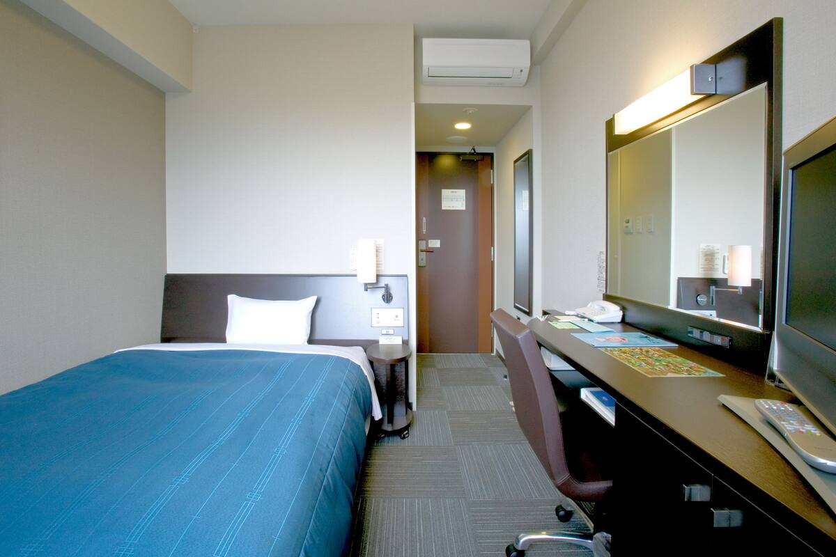 Ein Hotelzimmer mit einem Bett, einem Schreibtisch, einem Sessel, einem Spiegel und einem Fernseher.
