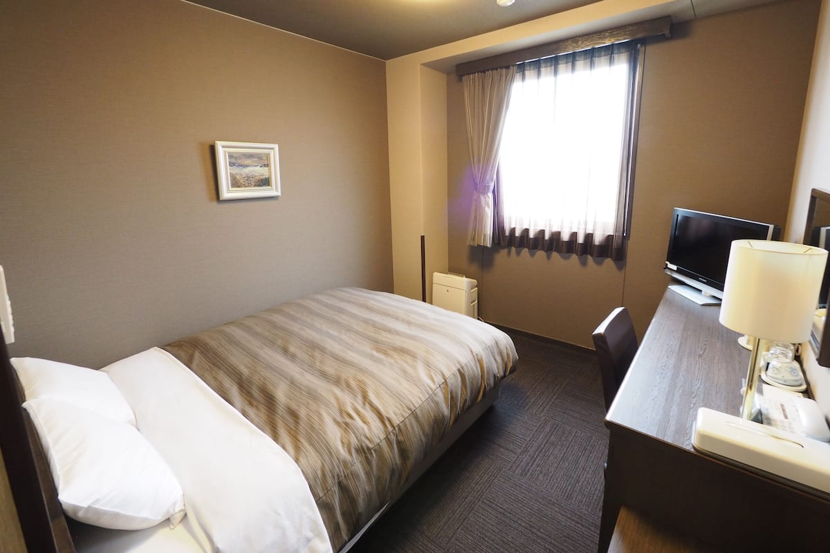 Een hotelkamer met een bed, een bureau met een lamp, een televisie en een foto aan de muur.