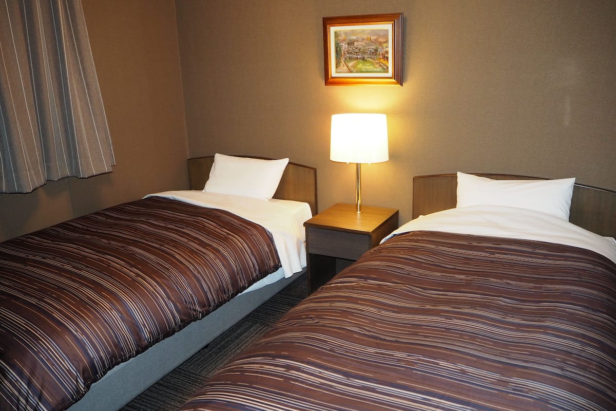 Een hotelkamer met twee enkele bedden, een nachtkastje met een lamp en een ingelijst schilderij aan de muur.