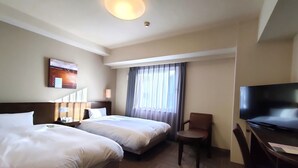 Une chambre d’hôtel avec deux lits, un bureau avec une chaise, une télévision et une fenêtre avec des rideaux.