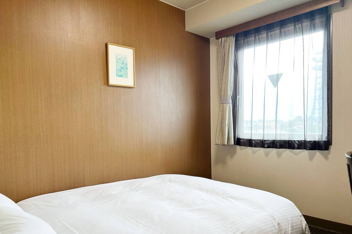 Une chambre d’hôtel avec un grand lit, un tableau encadré au mur et une fenêtre avec des rideaux.
