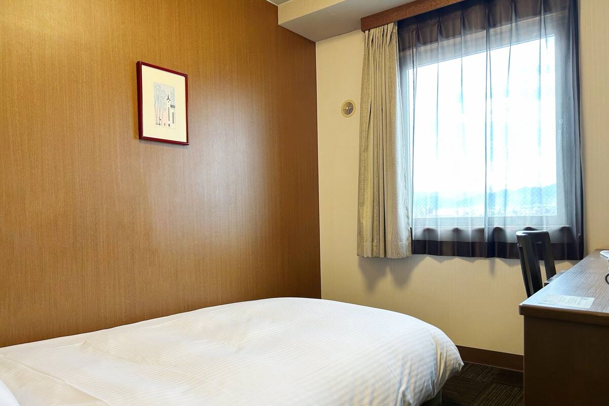 Une chambre d’hôtel avec un lit, un bureau et une fenêtre avec des rideaux.
