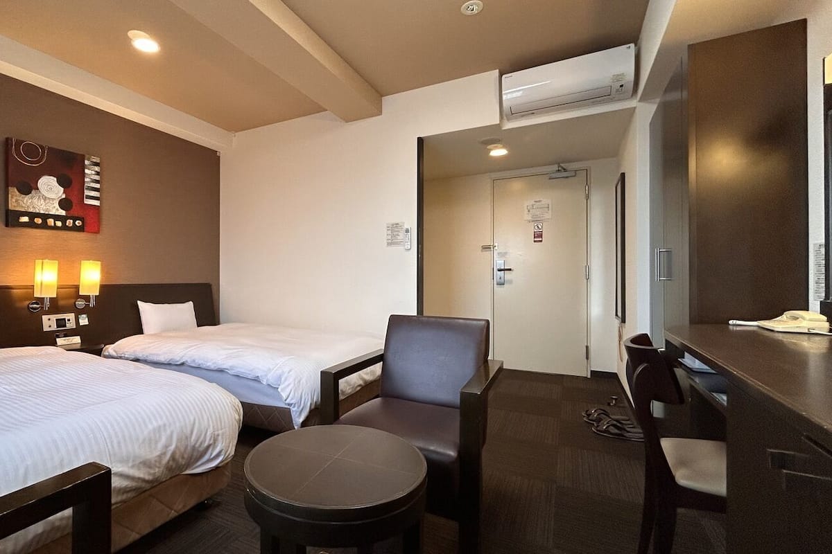 A hotel room with two beds, a desk, a chair, and a wall-mounted artwork.