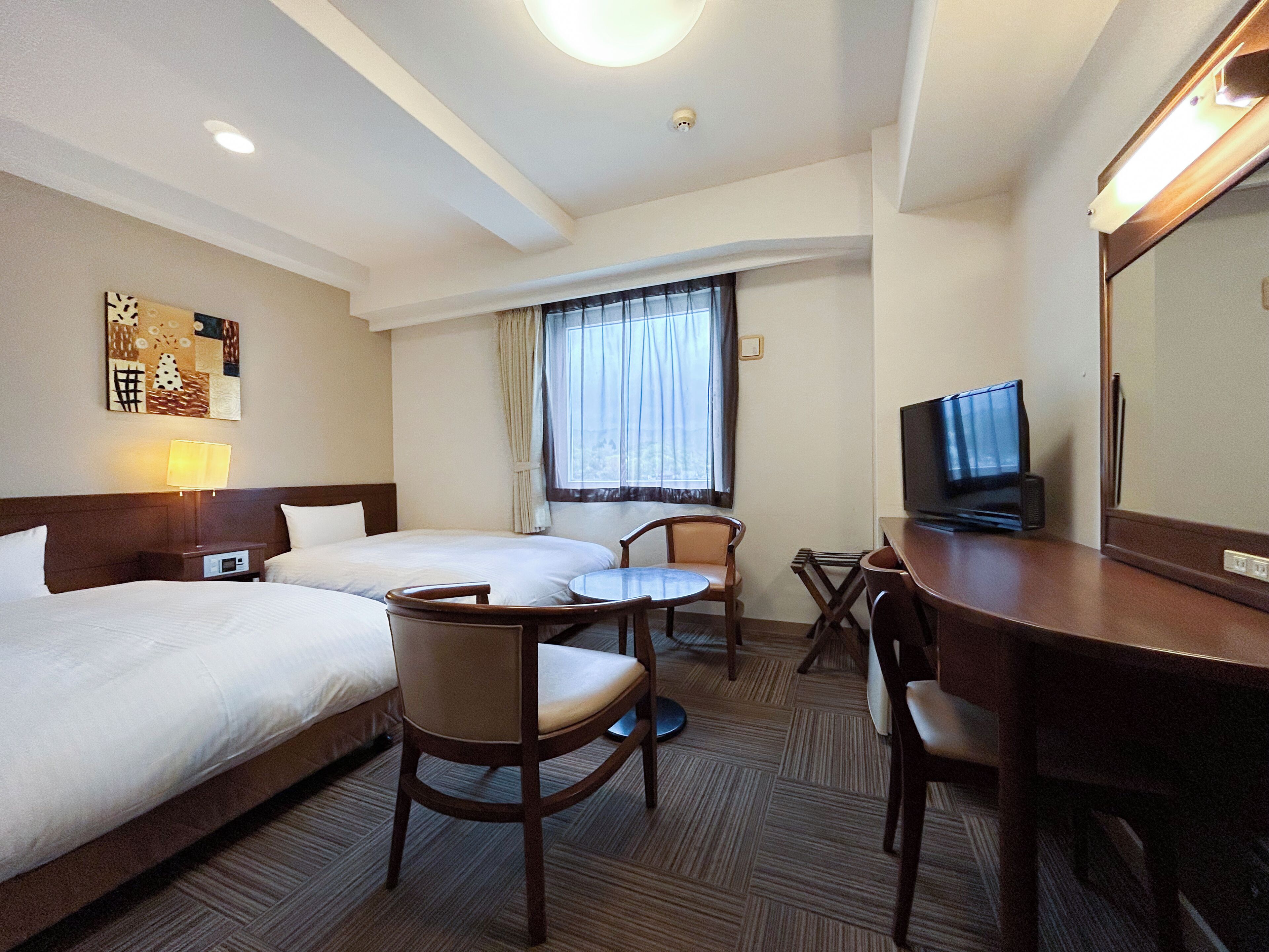 Habitación de hotel con dos camas, un escritorio, un televisor, una silla y una ventana con cortinas.