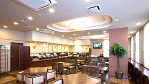 Un restaurante amplio con varias mesas y sillas, una barra que exhibe alimentos y un televisor en la pared.