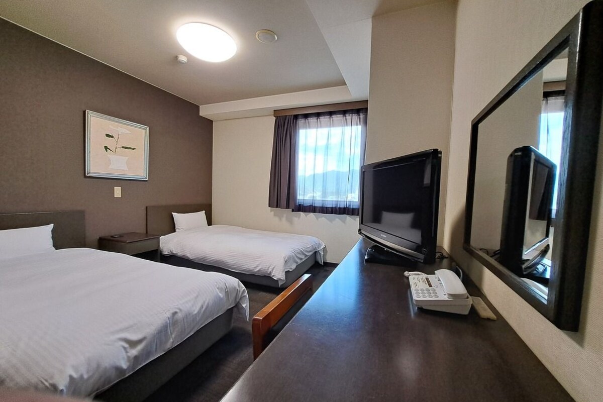 Una habitación de hotel con dos camas, televisión, teléfono y ventana con cortinas.