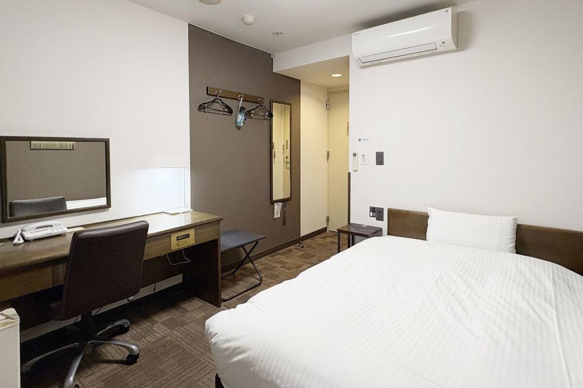 A hotel room with a bed, desk, chair, and a mirror.