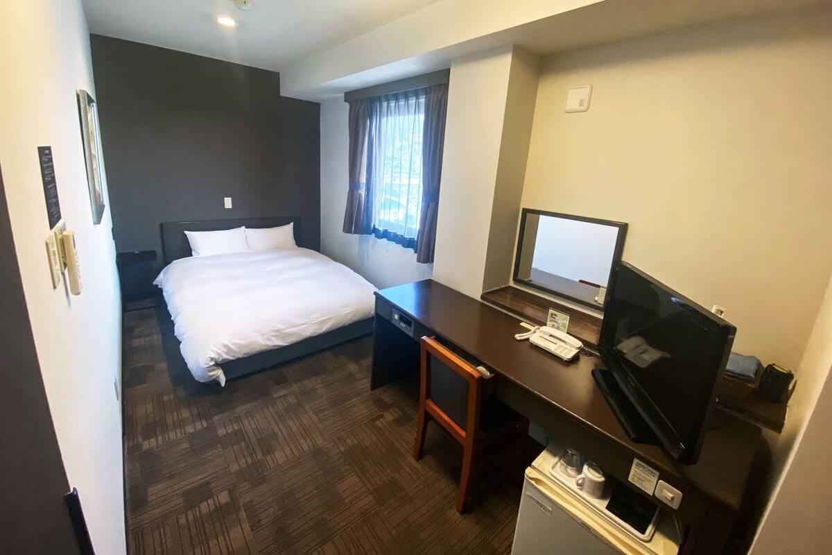 A hotel room with a bed, a desk with a computer, a television, and a refrigerator.