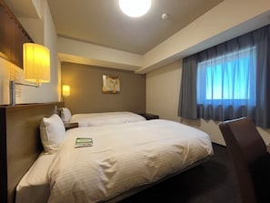 A hotel room with two beds, a desk, a chair, a lamp, and a window with curtains.