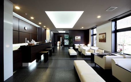 A modern hotel lobby with a reception desk, seating area, and large windows.