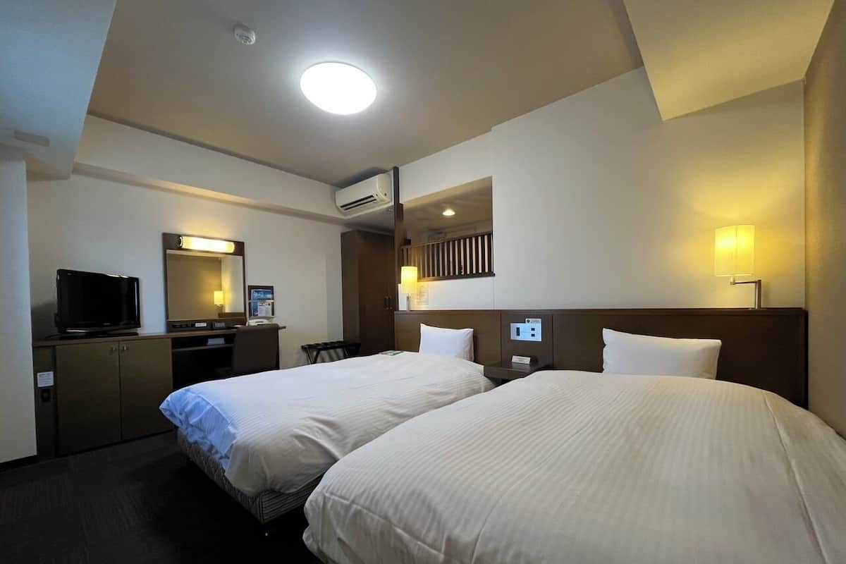 A hotel room with two beds, a desk with a computer, a television, and a mirror.