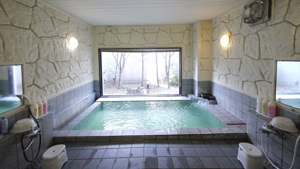 Une salle de bain aux murs en pierre, dotée d’une grande fenêtre, d’une baignoire et d’un espace douche.