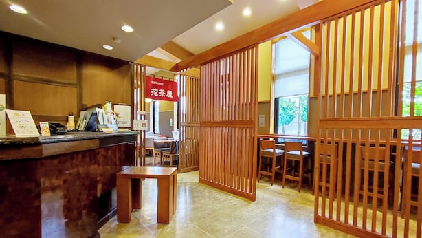 L’intérieur d’un restaurant, avec un comptoir d’accueil en bois, une salle à manger avec des tables et des chaises, et un panneau indiquant qu’il s’agit d’un restaurant.