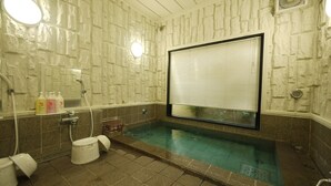 Une salle de bain avec un mur en pierre, une baignoire, des toilettes et un espace douche.