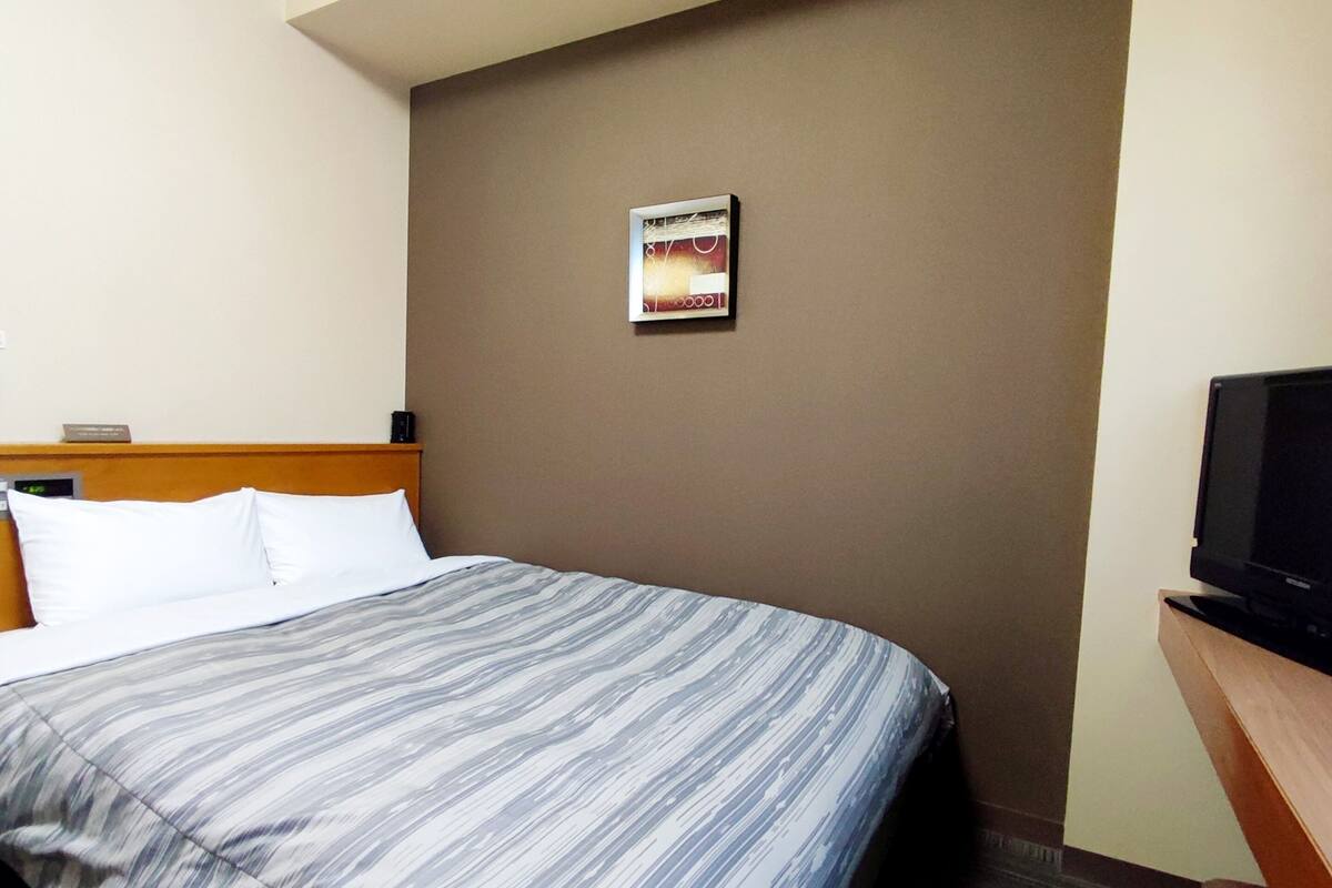 A hotel room with a bed, a television on a wooden stand, and a wall clock.