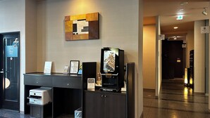 Una estación autoservicio para café con una máquina de café, un panel con el menú y un cubo de basura.