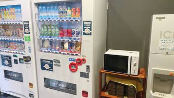 Máquinas expendedoras con diferentes bebidas y aperitivos, un microondas y una pequeña estantería con artículos.