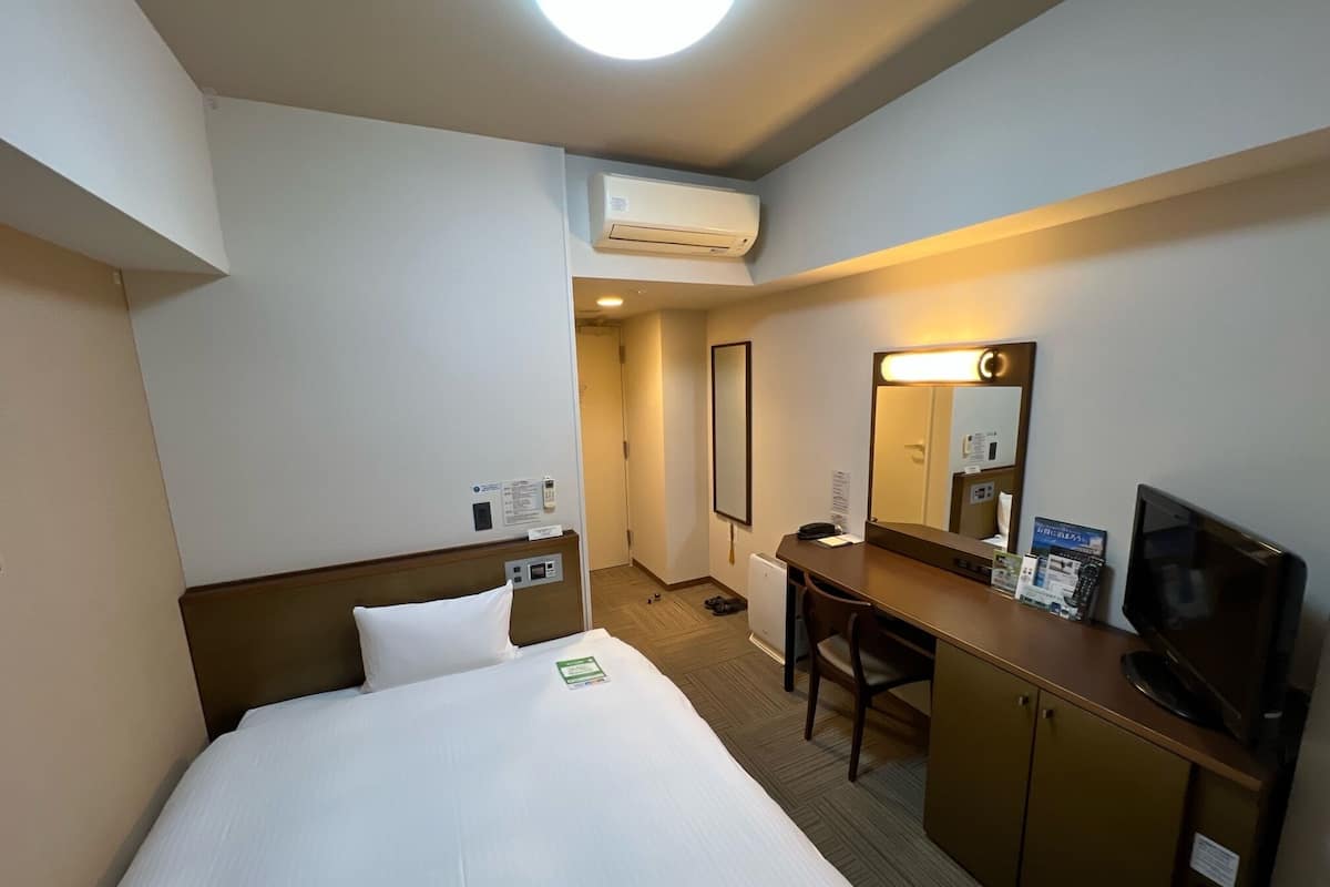 Ein Hotelzimmer mit Bett, Schreibtisch, Stuhl, Fernseher und Klimaanlage.