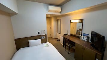 A hotel room with a bed, desk, chair, TV, and an air conditioning unit.