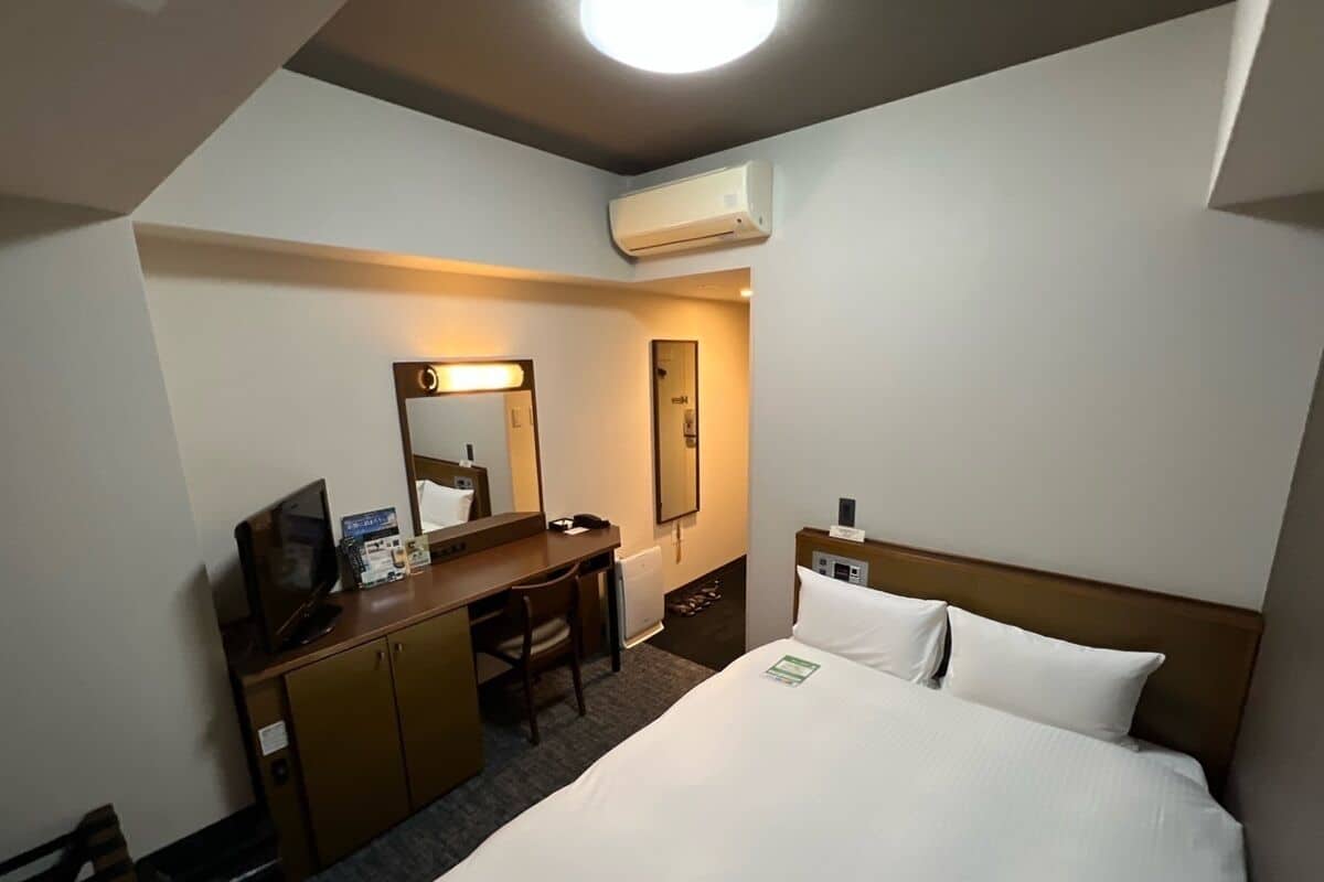 Ein Hotelzimmer mit einem Bett, einem Schreibtisch, einem Stuhl, einem Spiegel und einer Klimaanlage.