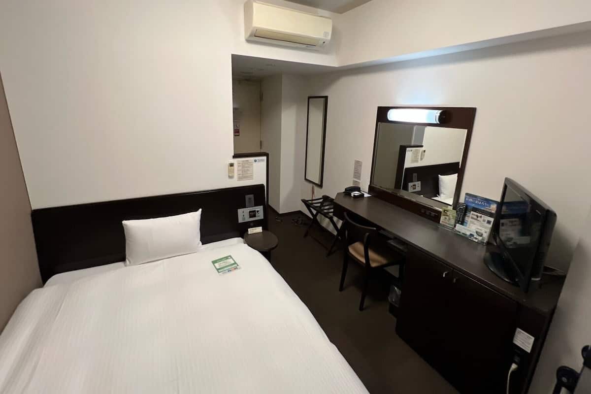 Ein Hotelzimmer mit Bett, Schreibtisch, Stuhl, Fernseher und Klimaanlage.