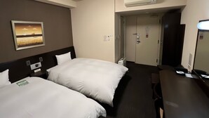 A hotel room with two beds, a desk, a mirror, an air conditioning unit, and a door leading to another room.