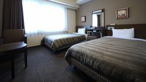 Une chambre d’hôtel avec deux lits, un bureau, une chaise et une grande fenêtre avec des rideaux.