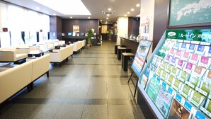 Un espace d’accueil d’hôtel comprenant un comptoir de réception, un coin salon avec des canapés et un présentoir de brochures.