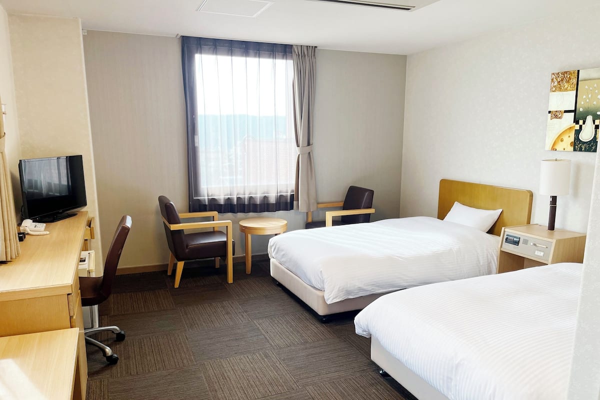 A hotel room with two beds, a desk with a computer, a chair, a small table, and a TV.