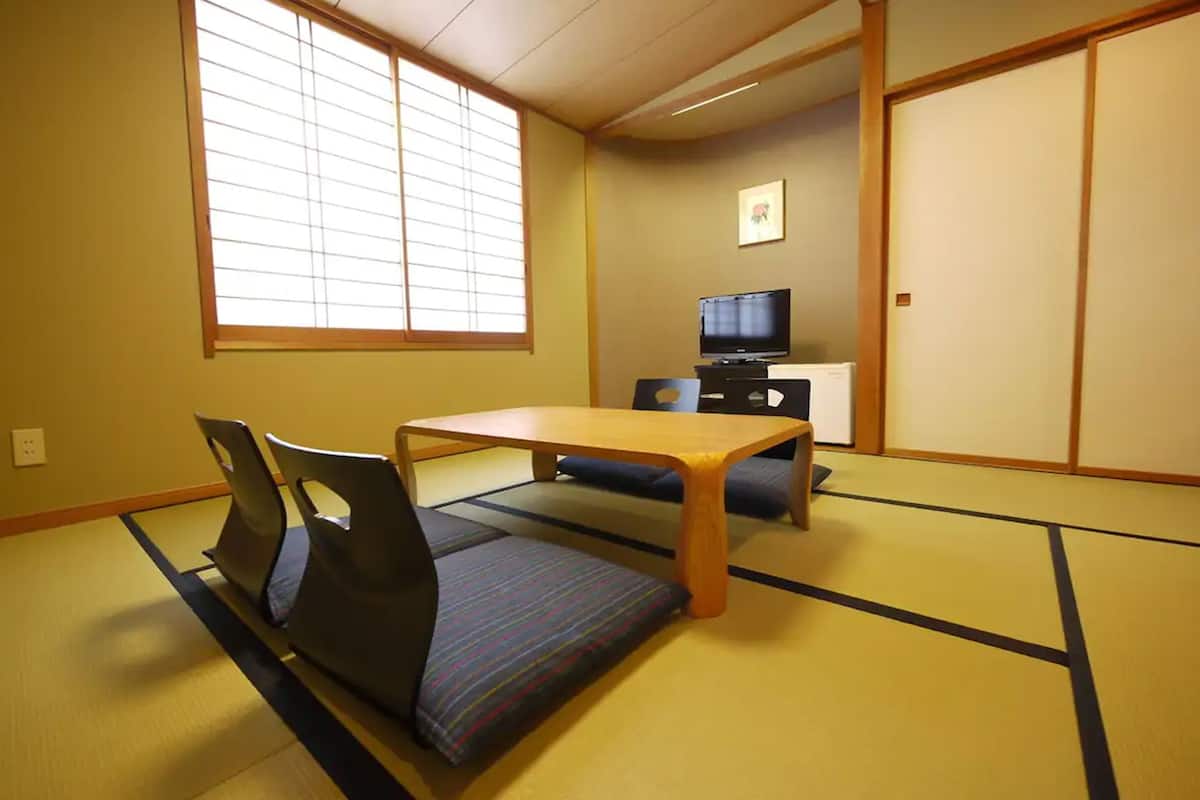 A tatami mat room with a low table and chairs, a television, and sliding doors.