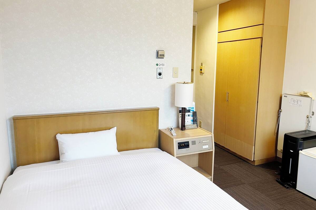 A hotel room with a bed, a bedside table with a lamp, a phone, and a minibar.