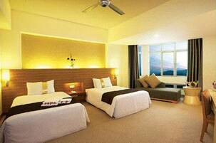 Habitación de hotel con dos camas, un sofá, una ventana con cortinas y un ventilador de techo.