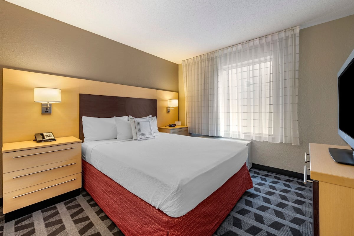 A hotel room with a large bed, bedside tables with lamps, a TV, and a window with sheer curtains.