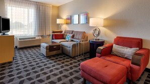 Habitación de hotel con sofá, sillón, televisión, aire acondicionado y una obra de arte en la pared.