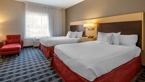 Habitación de hotel con dos camas, un sillón rojo, una mesita de noche con lámpara y una ventana con cortinas.