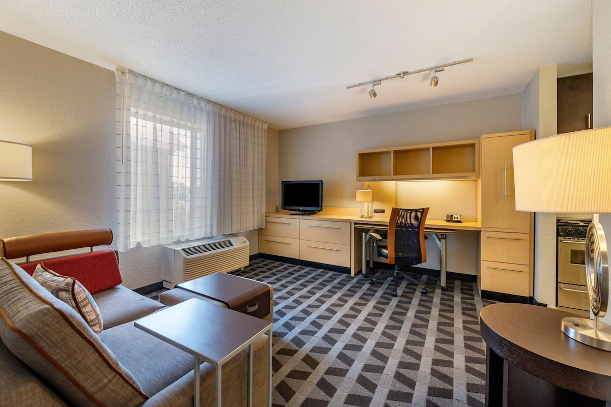 A hotel room with a sofa, a desk, a television, a lamp, and a kitchen area.