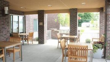 An outdoor patio area with brick walls, wooden tables and chairs, and a view of the street.
