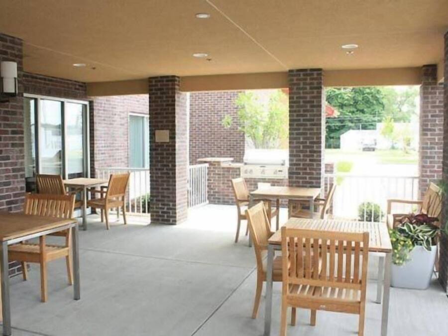 An outdoor patio area with brick walls, wooden tables and chairs, and a view of the street.