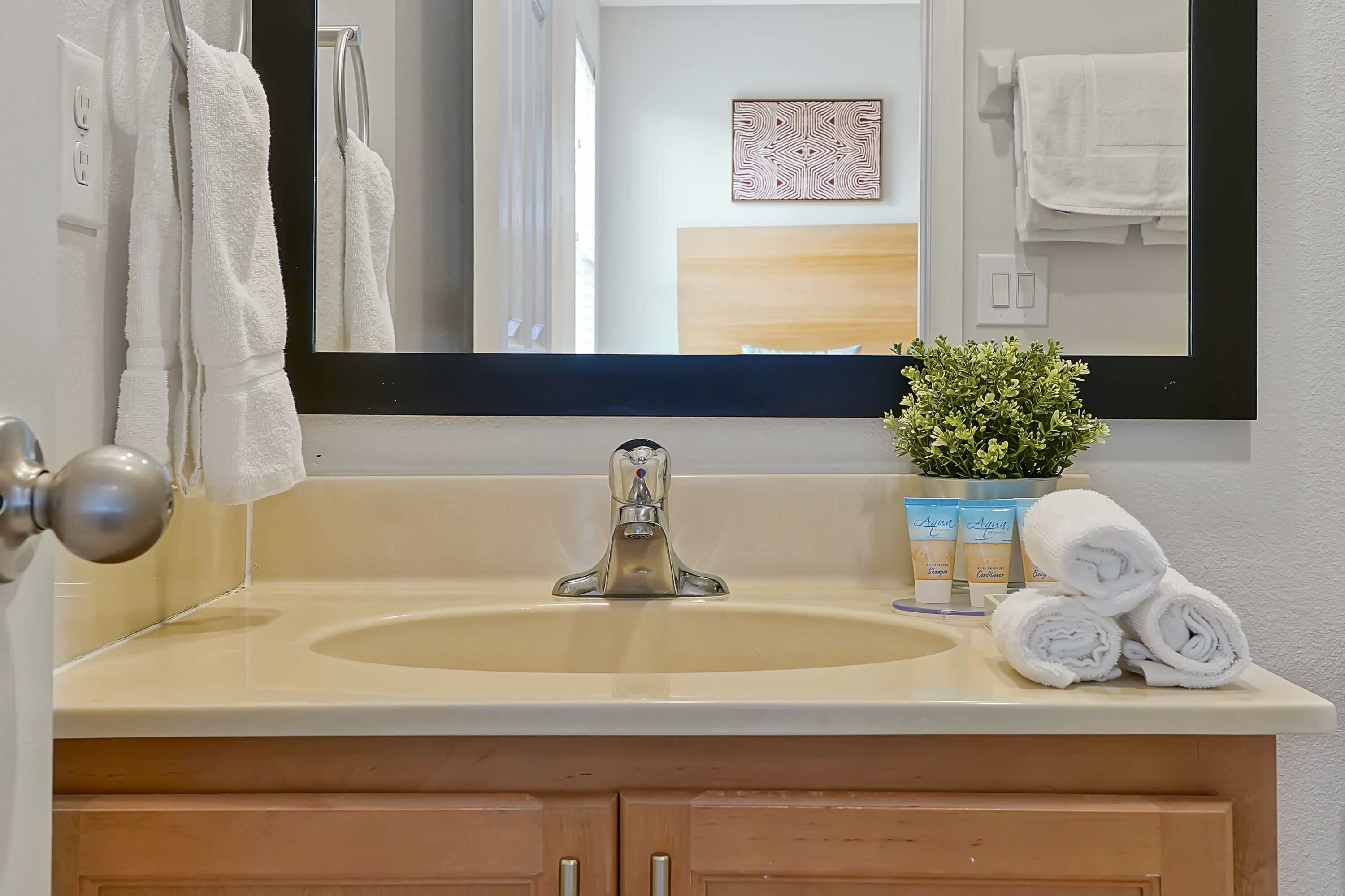 A bathroom with a beige sink, a mirror, a towel rack, a potted plant, and a cabinet.