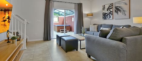 A modern living room with a grey sofa, wooden coffee table, and a view through a glass door to an outdoor area.