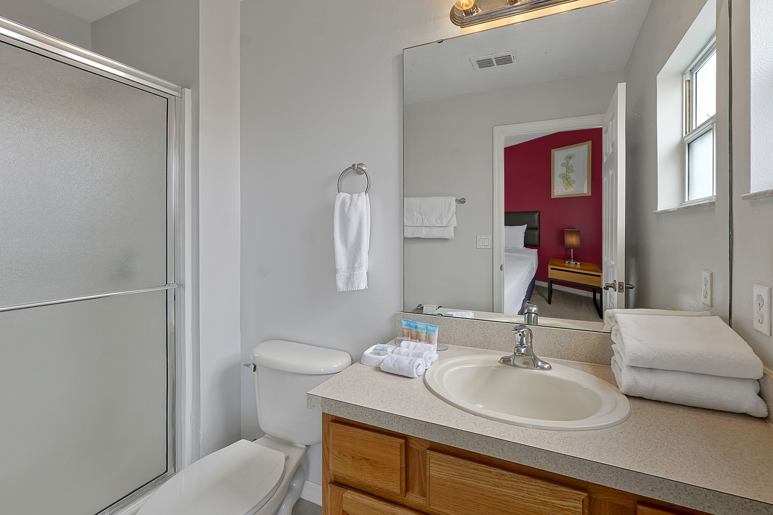 A bathroom with a white sink, mirror, and toilet. There are towels and toiletries on the counter.