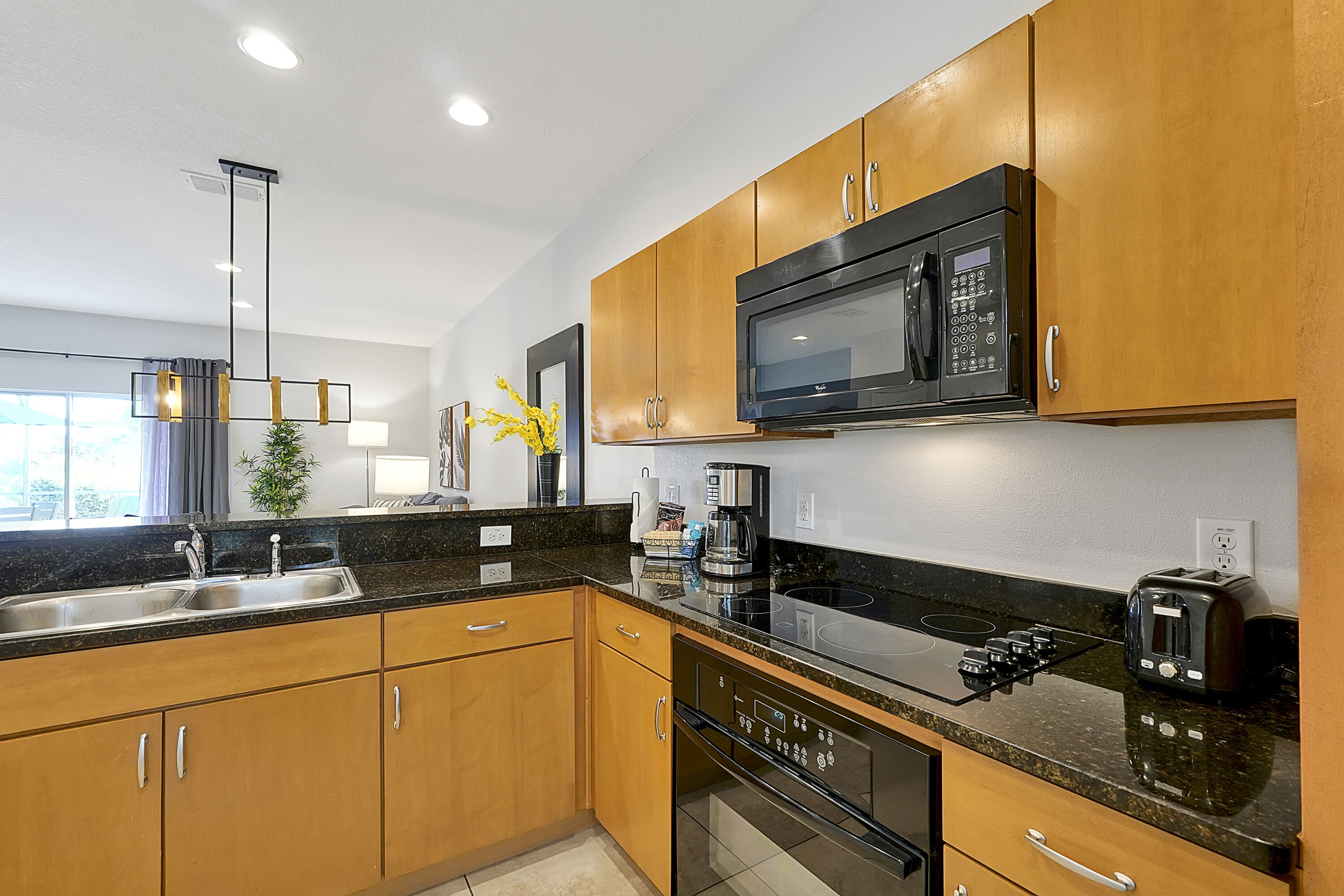 A modern kitchen with wooden cabinets, a black microwave, a stove, and a sink.