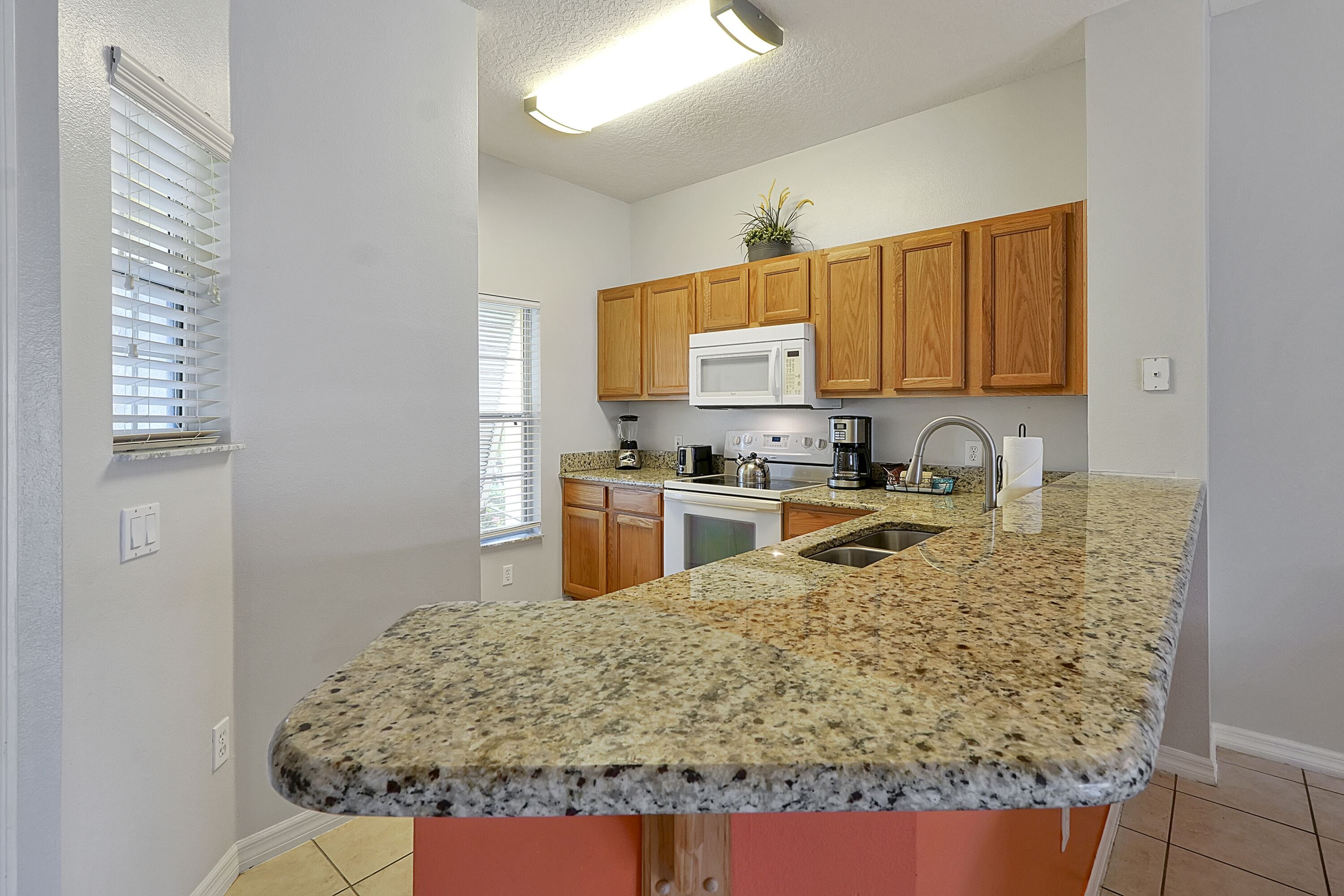 A kitchen with granite countertops, wooden cabinets, a microwave, and a sink.