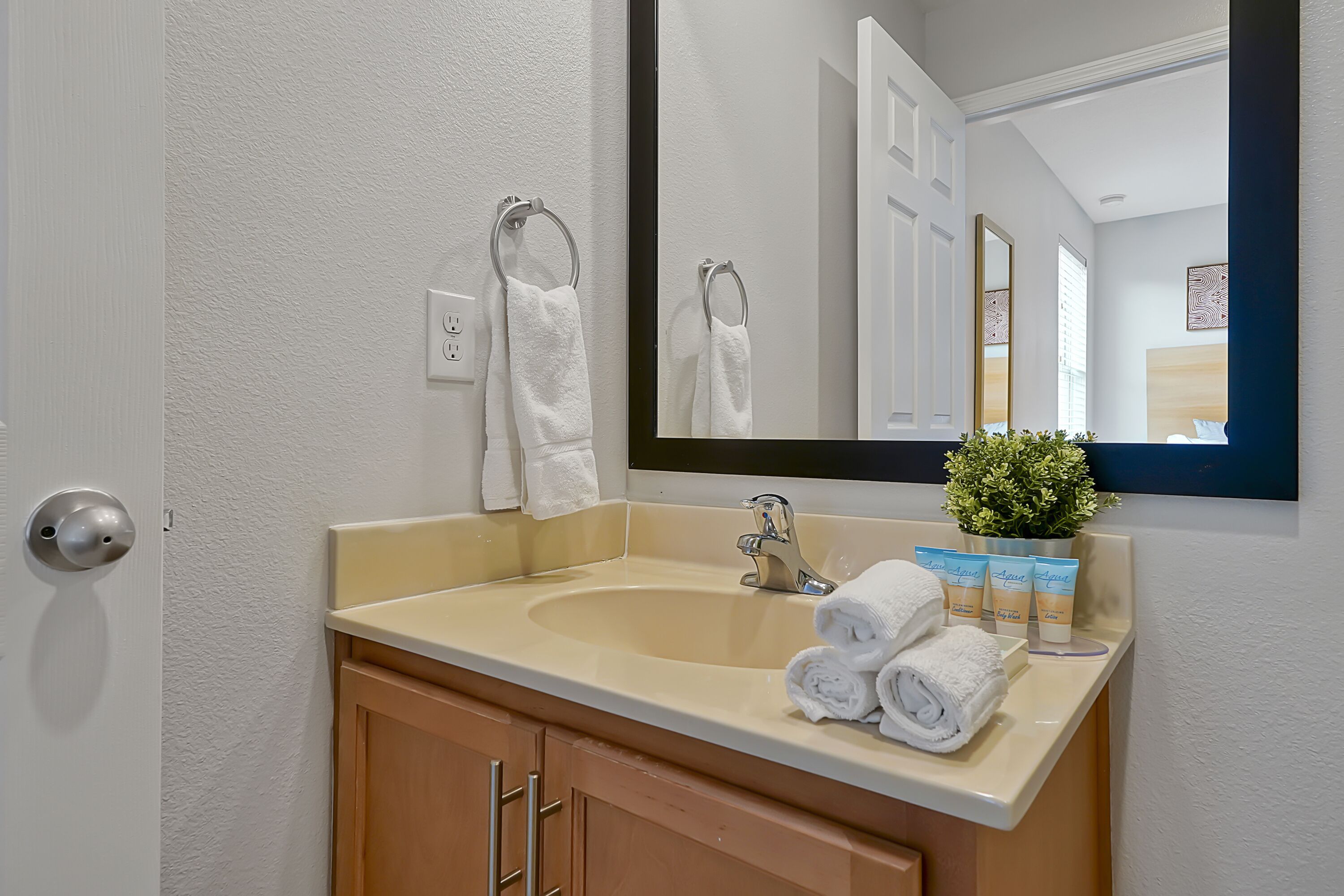 A bathroom with a beige sink, a large mirror, and a potted plant on the counter.