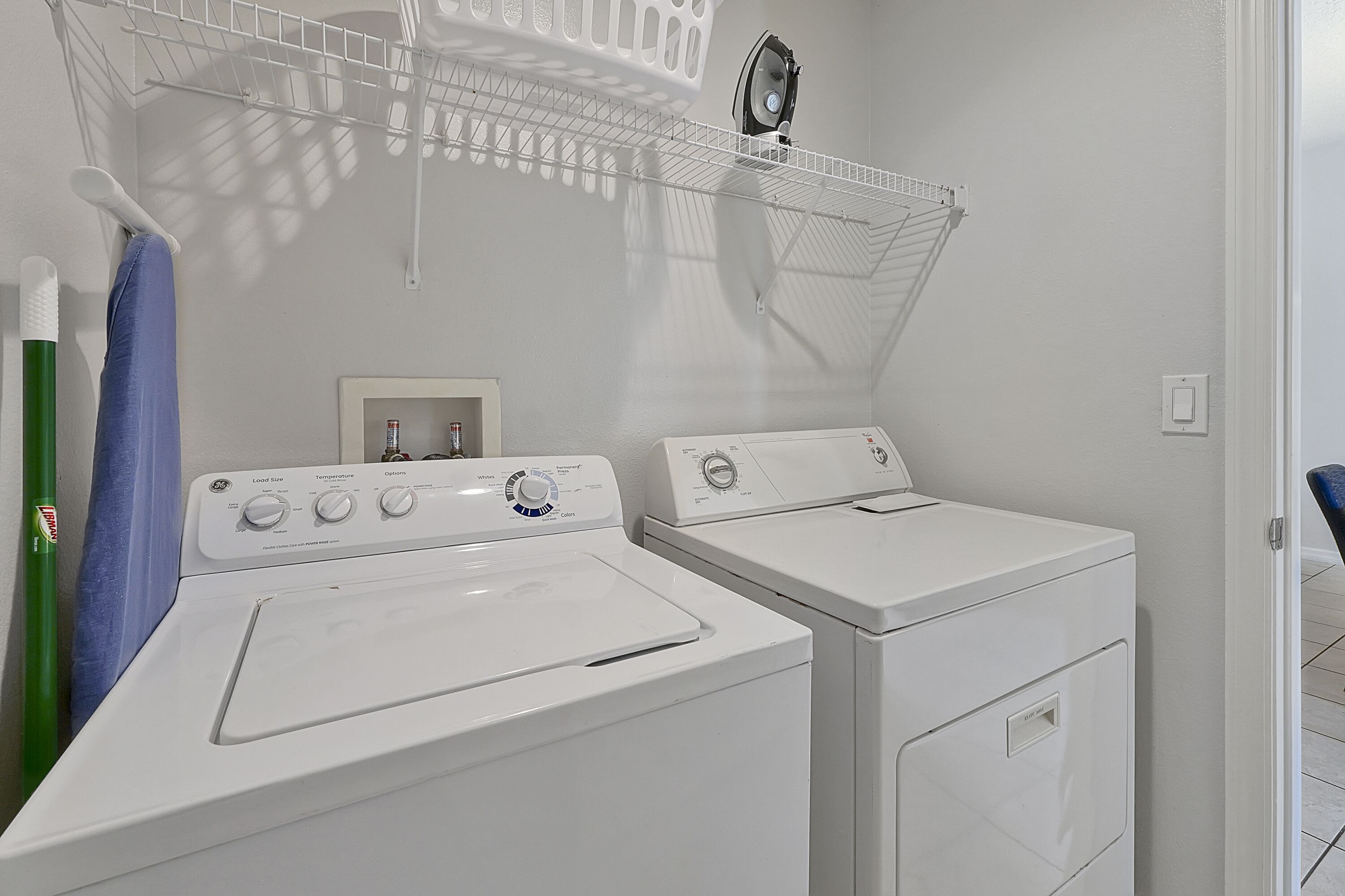 A laundry area with two front-loading washing machines, a drying rack, and a small shelf with a fan.