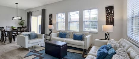 A modern living room with a white sofa, a coffee table, and a dining area with a table and chairs.