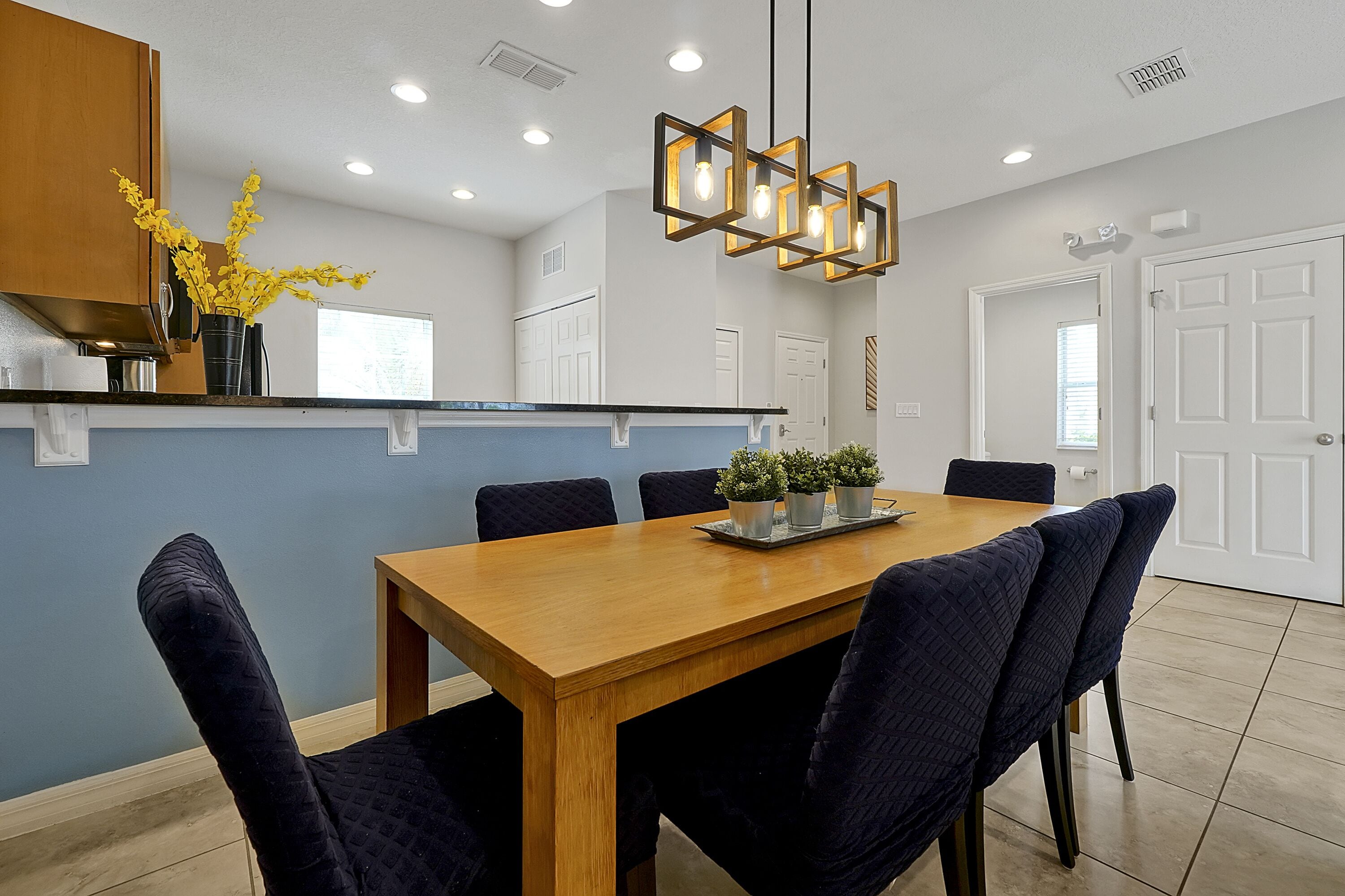 A modern dining area with a wooden table, dark upholstered chairs, and a decorative light fixture.