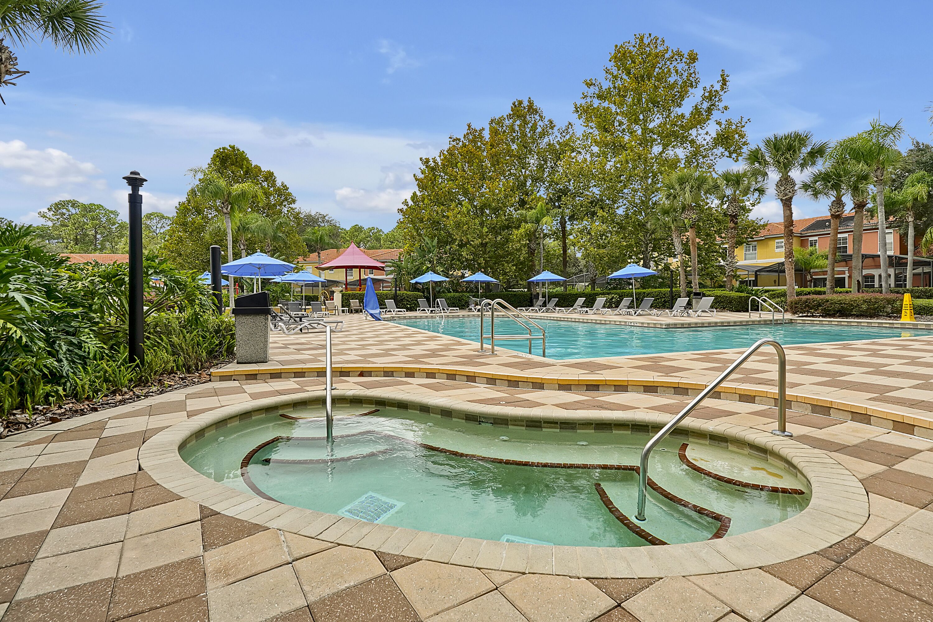 A swimming pool with a checkered tile deck, lounge chairs, and umbrellas.