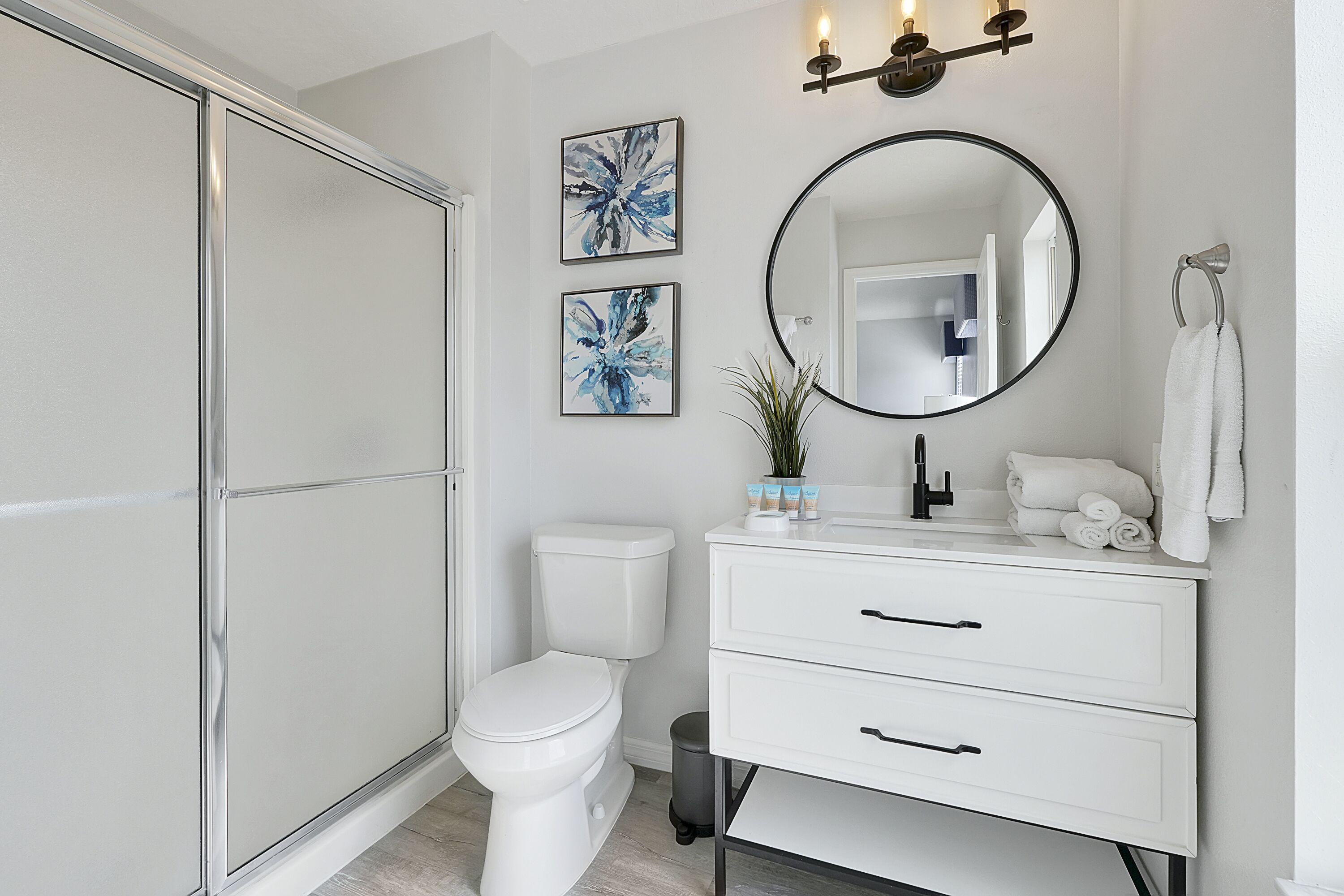 A modern bathroom with a toilet, a vanity with drawers, a mirror, and two abstract art pieces on the wall.