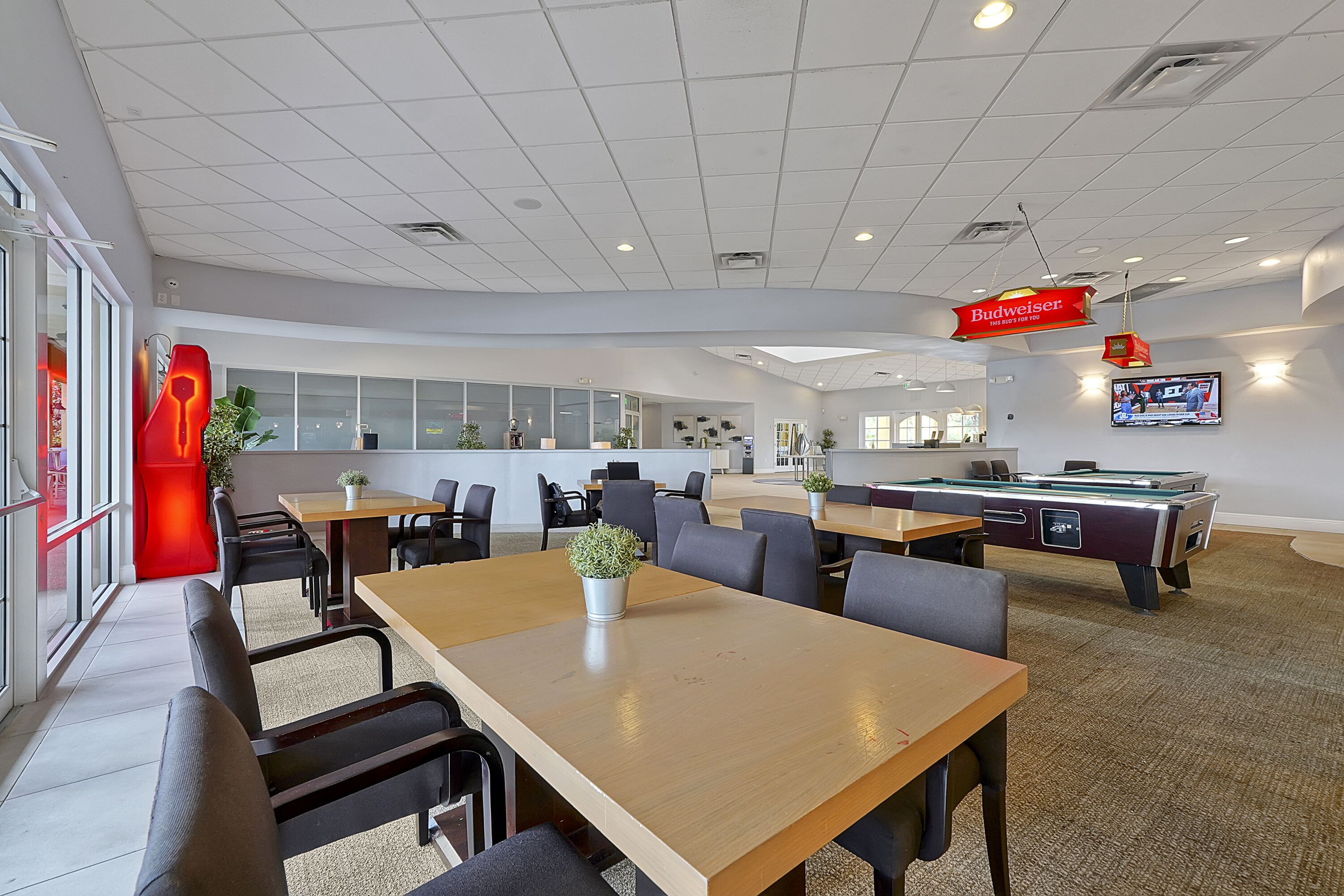 A modern lounge area with tables, chairs, a pool table, and a television screen.
